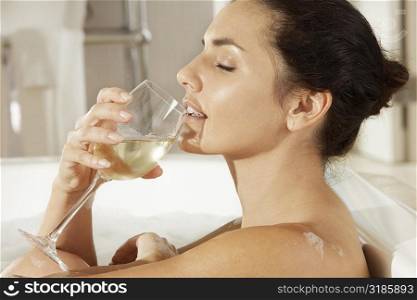 Side profile of a young woman drinking white wine in a bathtub