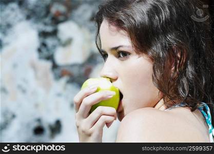 Side profile of a young woman eating a green apple