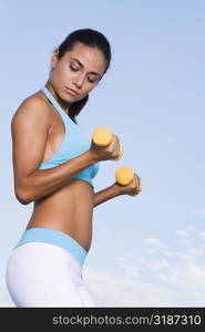 Side profile of a young woman exercising with dumbbells