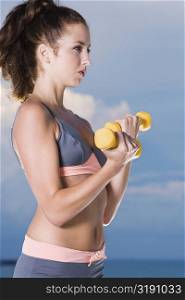 Side profile of a young woman exercising with dumbbells