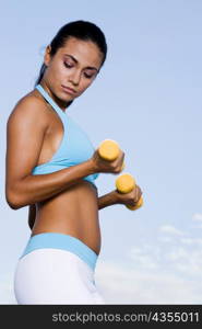 Side profile of a young woman exercising with dumbbells