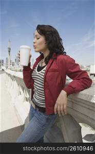 Side profile of a young woman holding a disposable glass of coffee