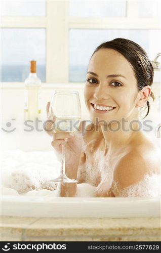 Side profile of a young woman holding a glass of wine in a bathtub
