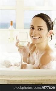 Side profile of a young woman holding a glass of wine in a bathtub
