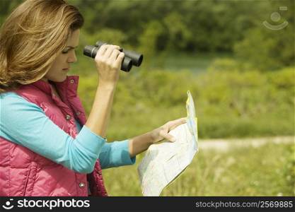 Side profile of a young woman holding a map and a pair of binoculars