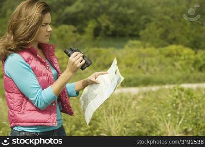 Side profile of a young woman holding a map and a pair of binoculars