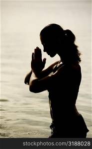 Side profile of a young woman in a prayer position in the lake