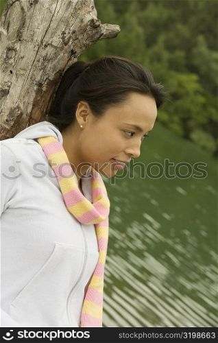 Side profile of a young woman leaning against a tree trunk by the lake
