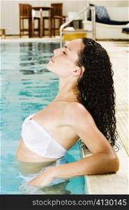 Side profile of a young woman leaning at the edge of a swimming pool