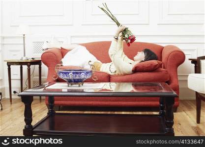 Side profile of a young woman lying on a couch and holding a bunch of flowers