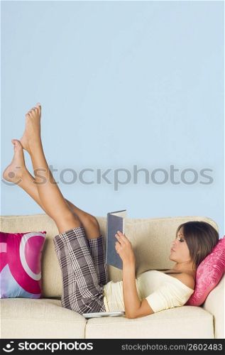 Side profile of a young woman lying on a couch and reading a book
