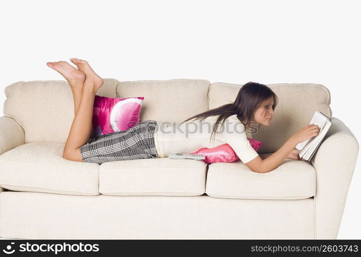 Side profile of a young woman lying on a couch and reading a book