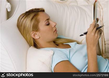 Side profile of a young woman lying on a couch reading a book