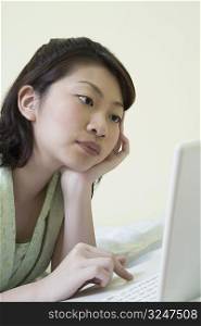 Side profile of a young woman lying on the bed and using a laptop