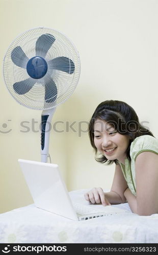 Side profile of a young woman lying on the bed and using a laptop