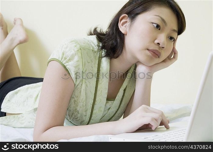 Side profile of a young woman lying on the bed and using a laptop