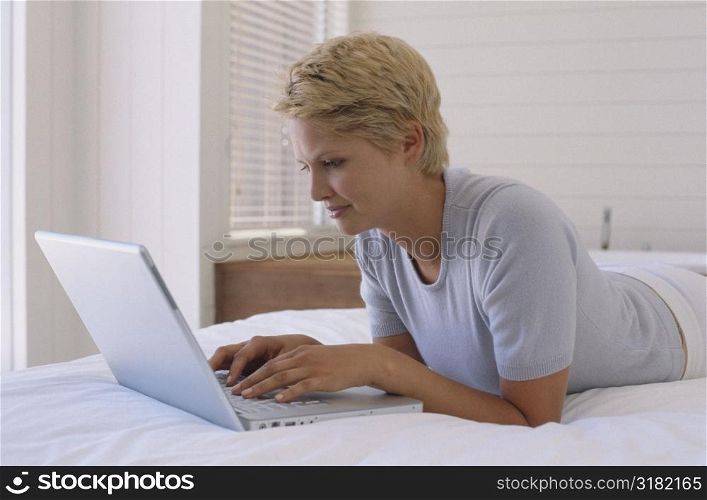 Side profile of a young woman lying on the bed with a laptop
