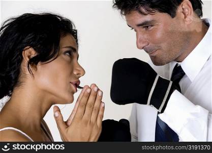 Side profile of a young woman pleading before a mid adult man wearing boxing gloves