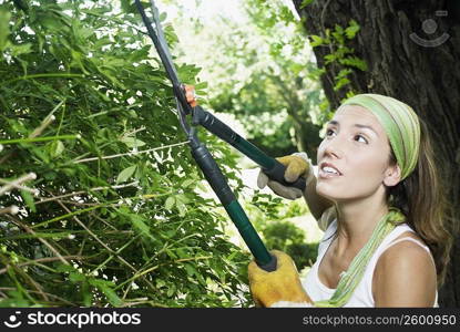 Side profile of a young woman pruning with hedge clippers