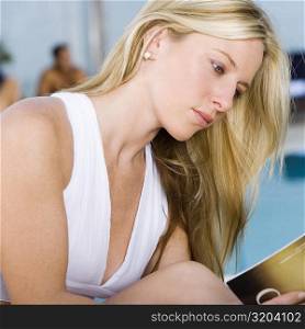 Side profile of a young woman reading a book at the poolside