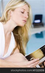 Side profile of a young woman reading a book at the poolside