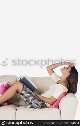 Side profile of a young woman reclining on a couch and holding a book
