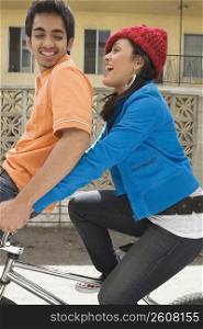 Side profile of a young woman riding a bicycle with a young man sitting on the handlebar