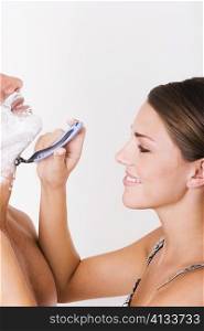 Side profile of a young woman shaving a mid adult man
