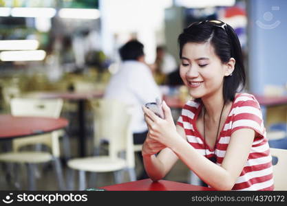 Side profile of a young woman sitting in a restaurant and using a mobile phone