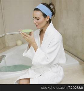 Side profile of a young woman sitting near a bathtub and smelling a dish of bath crystals