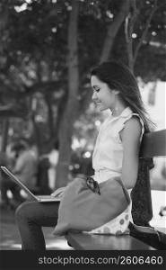 Side profile of a young woman sitting on a bench and using a laptop, Old San Juan, San Juan, Puerto Rico