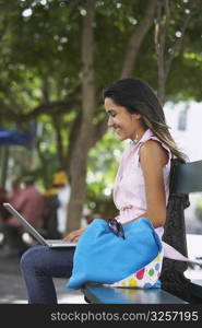 Side profile of a young woman sitting on a bench and using a laptop, Old San Juan, San Juan, Puerto Rico