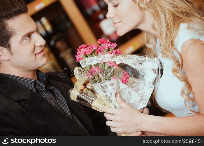 Side profile of a young woman smelling a bouquet of flowers in front of a young man