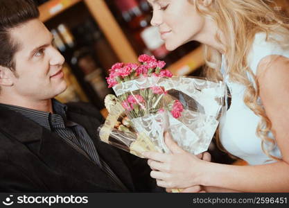 Side profile of a young woman smelling a bouquet of flowers in front of a young man