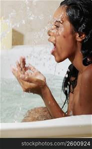 Side profile of a young woman splashing water on her face in a bathtub