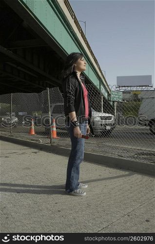 Side profile of a young woman standing under an overpass holding a mobile phone