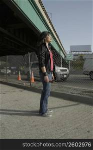 Side profile of a young woman standing under an overpass holding a mobile phone