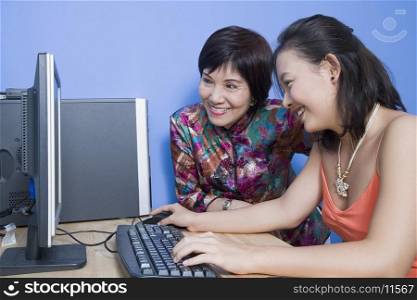 Side profile of a young woman using a computer with her mother sitting beside her
