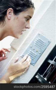 Side profile of a young woman using a doorbell