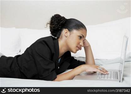 Side profile of a young woman using a laptop on the bed