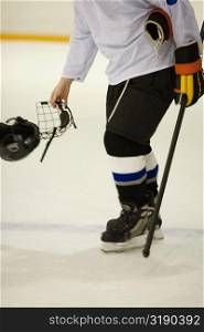 Side profile of an ice hockey player holding an ice hockey skate and a helmet