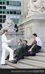 Side profile of four businessmen and a businesswoman discussing on steps