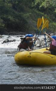 Side profile of four people rafting in a river