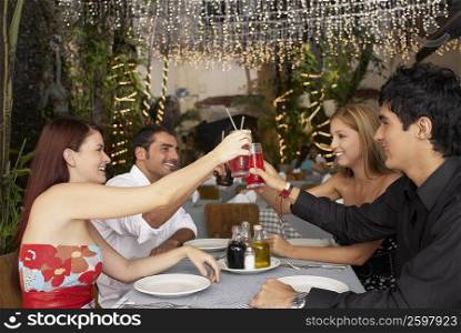 Side profile of four people sitting at a table and toasting with glasses