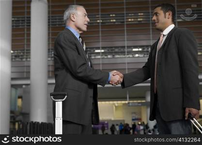 Side profile of two businessmen shaking hands at an airport lounge