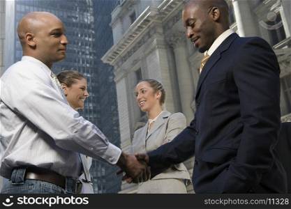 Side profile of two businessmen shaking hands with two businesswomen smiling
