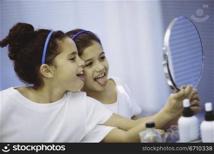 Side profile of two girls looking in a mirror making faces