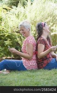 Side profile of two mature women sitting back to back in a park and listening to MP3 players