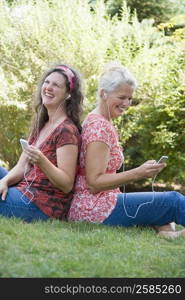 Side profile of two mature women sitting back to back in a park and listening to MP3 players