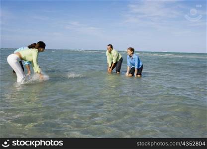 Side profile of two mid adult couples splashing water on each other on the beach